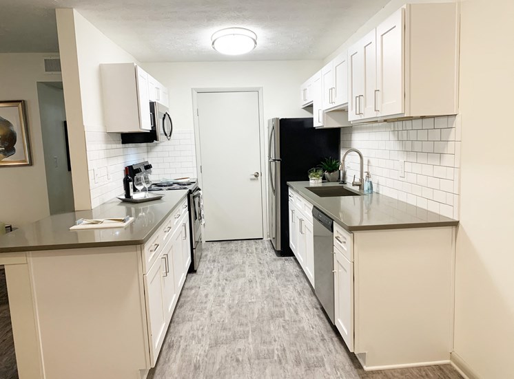 Cook in your gourmet kitchen at Icon Avondale. White cabinets, stainless steel appliances, fridge, microwave, oven, dishwasher, sink, and light flooring and gray countertops.